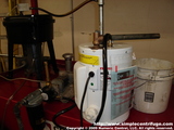 This is the current setup using a 2.5 gallon water heater. The oil enters on the cold side and exits the hot side. The exit is plumbed to a T with a length extending higher than the centrifuge (or feed tank). This allows water vapor to escape. Be careful not to turn up the thermostat too high or the safety valve will open, note the bucket just in case.